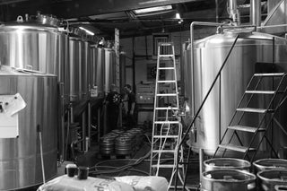 Two brewers working inside Hammerton Brewery, surrounded by stainless steel tanks and brewing equipment.
